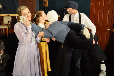 Image: A kiss — Agnes (Anney Haws) and Tootie (Alyssa Carey) with their affectionate dummy and an angry Conductor (Max Benson).