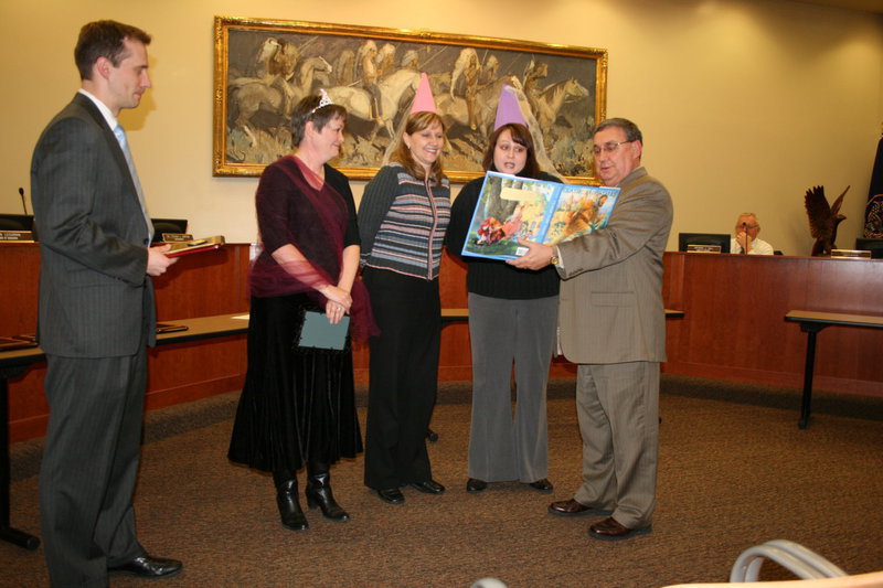 Image: Fairy Tale — Principal Maria Nelson (pink hat) and kindergarten teacher Jennifer Jones (purple hat) read a fairy tale to “princess” Julie Allgood (tiara) about her hard work and dedication at Millville elementary school.